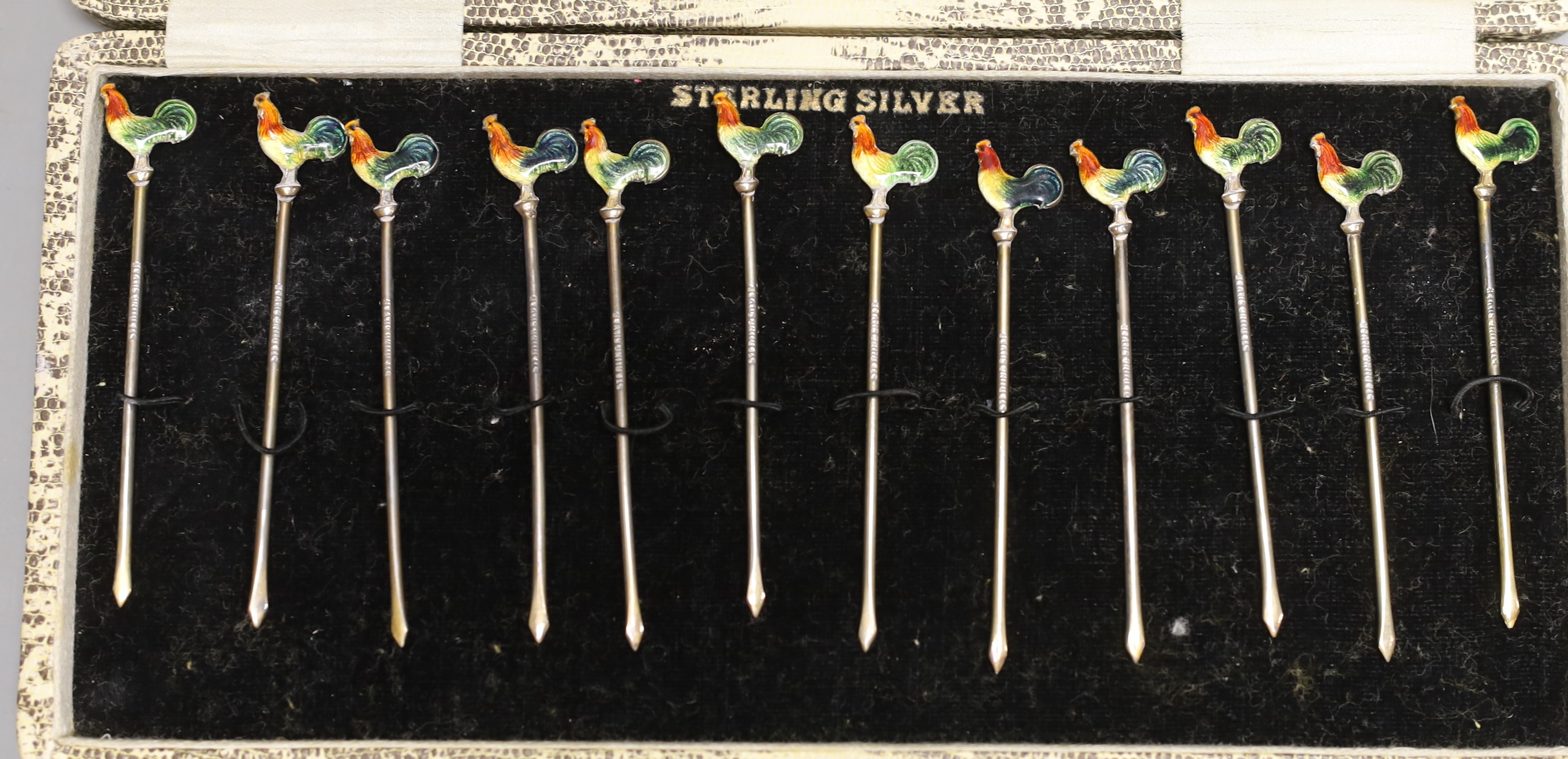 A cased set of twelve sterling and polychrome enamel cocktail sticks, the terminals modelled as cockerels, 80mm.